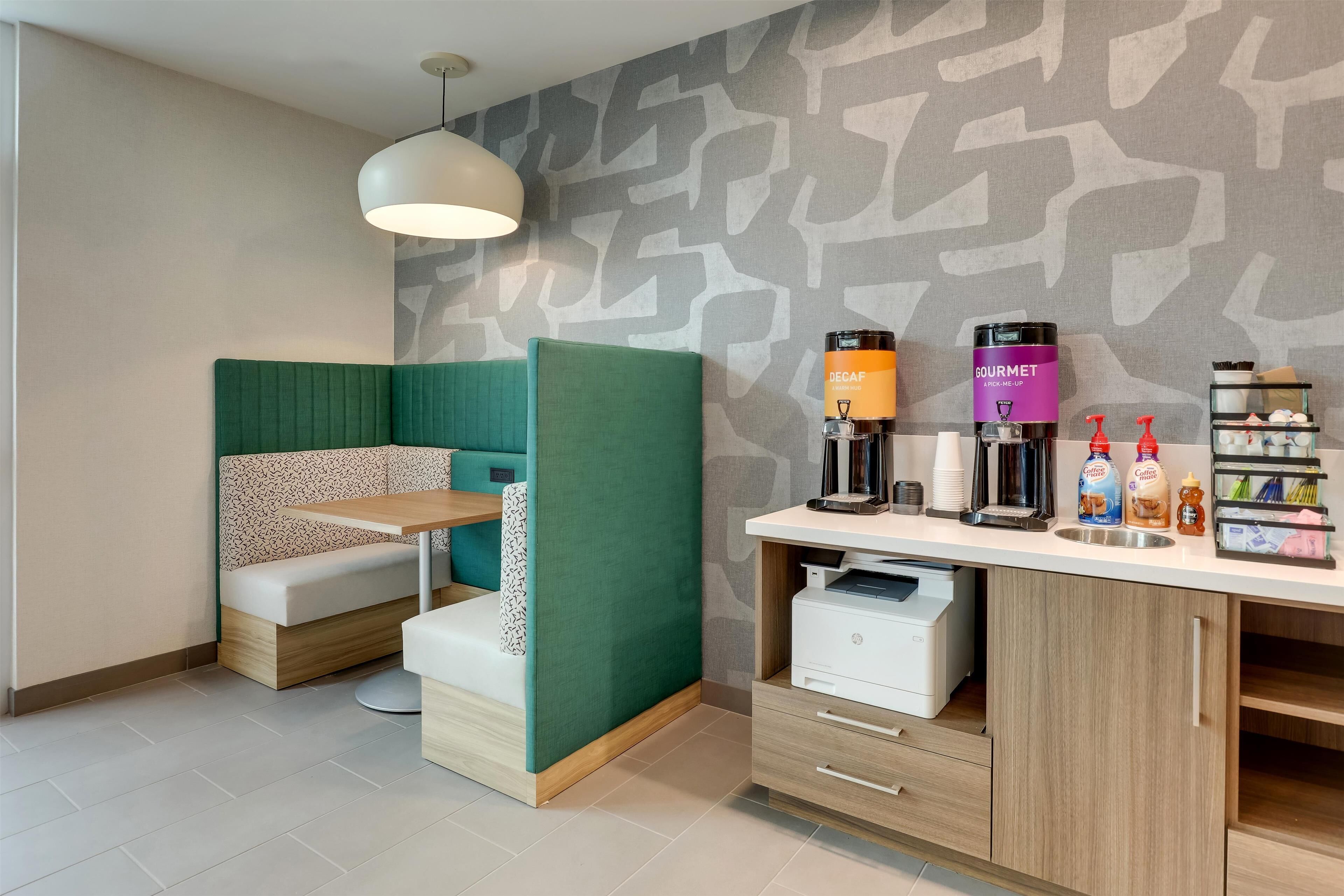 A modern room with a green partition, a wooden desk with a printer, and a coffee station.