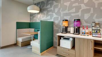 A modern room with a green partition, a wooden desk with a printer, and a coffee station.