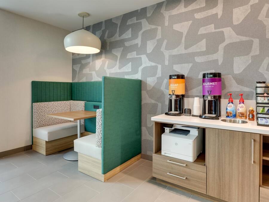 A modern room with a green partition, a wooden desk with a printer, and a coffee station.