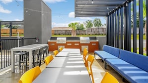 An outdoor patio with a long table, yellow chairs, a blue sofa, and a barbecue grill. - Home2 Suites By Hilton Crestview I-10 (Crestview)