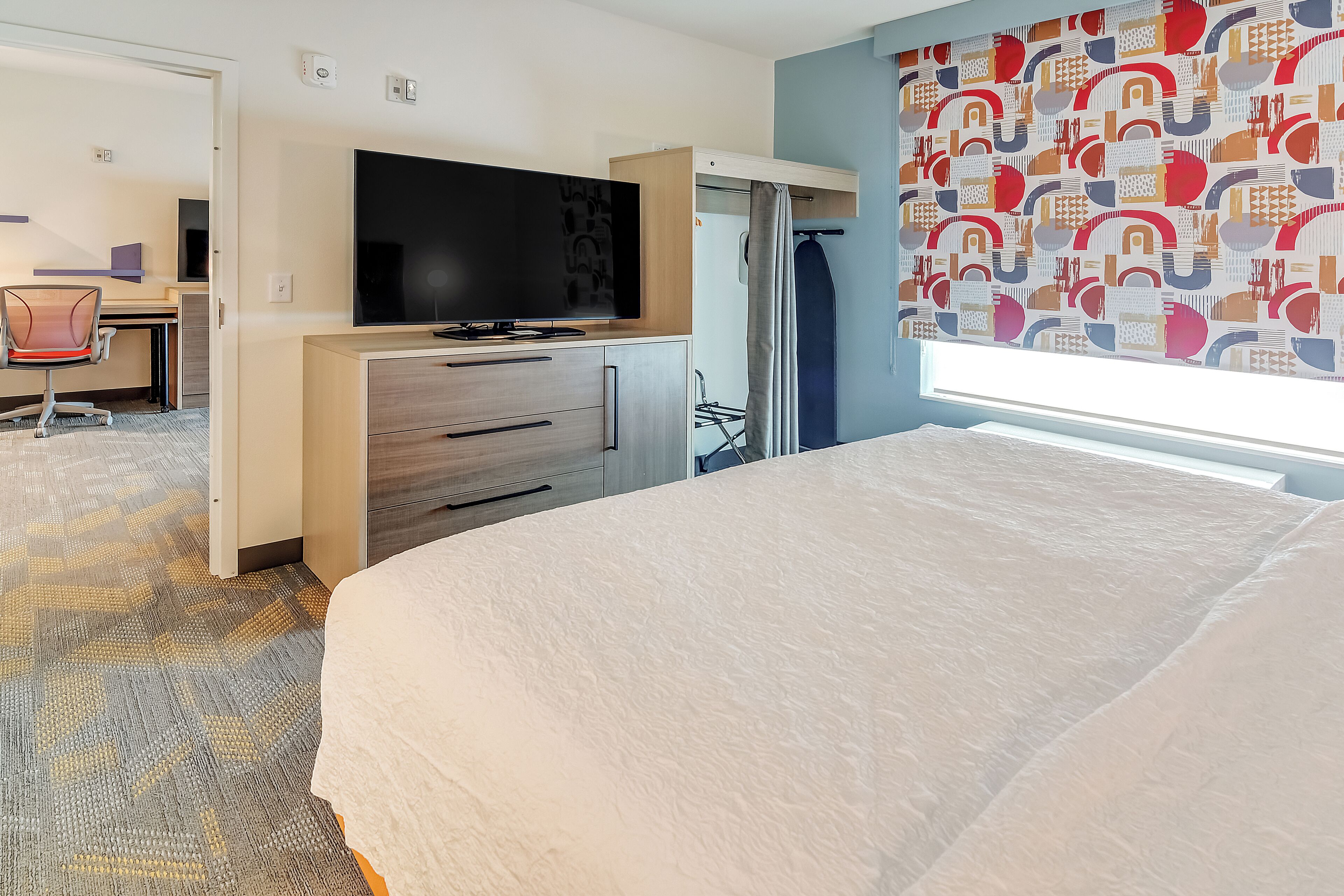 Una habitación de hotel con una cama, un escritorio con una silla, un televisor y una pared con diseño.