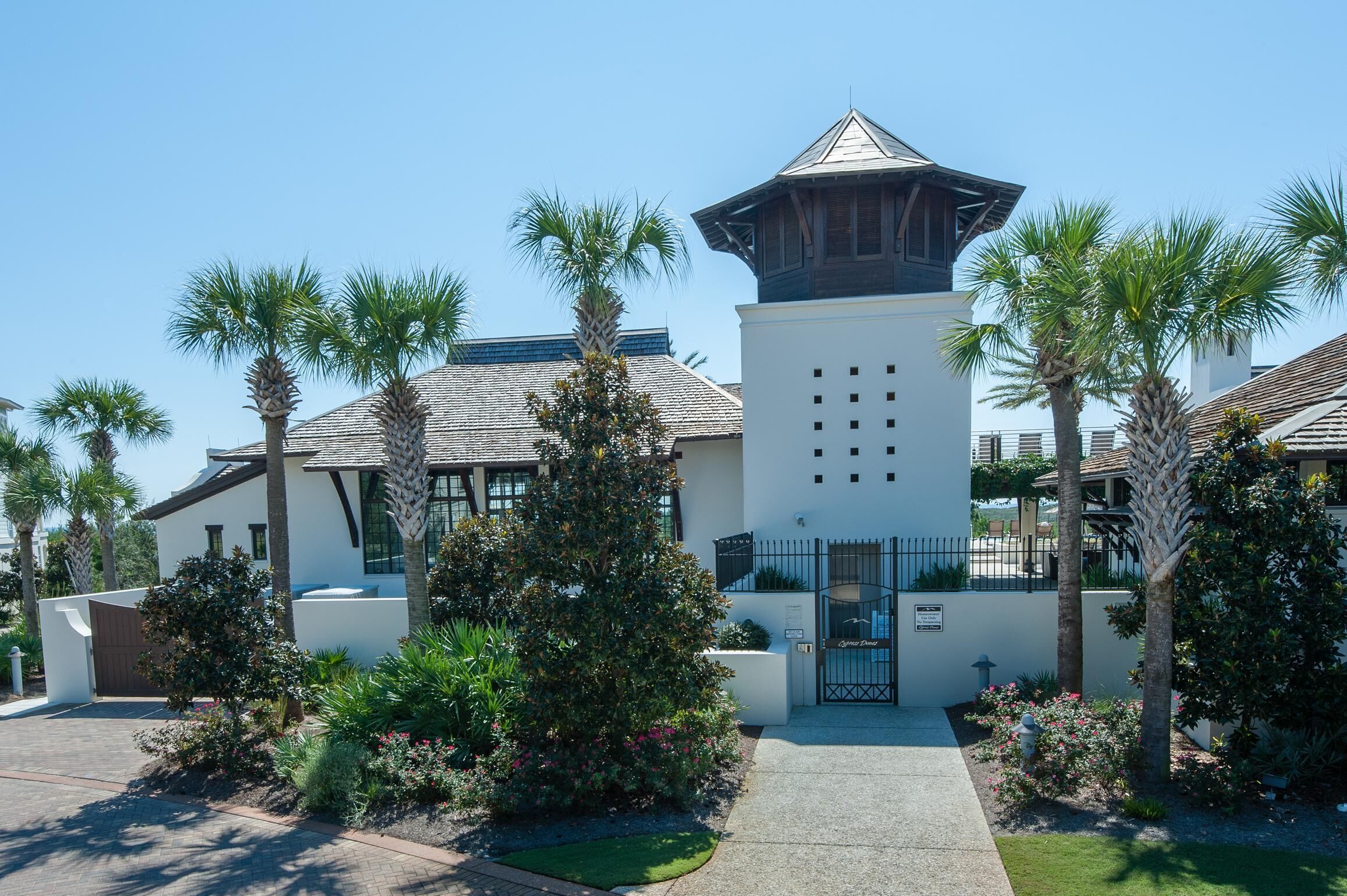 A modern building with a central tower, surrounded by palm trees and well-maintained gardens.