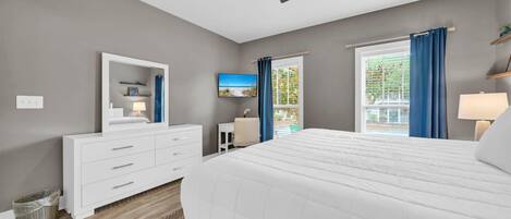 Quarto com cama grande, ventoinha no teto, escrivaninha e janela com cortinas.