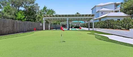 A golf course with a covered pavilion, a wooden fence, and a building with a balcony.
