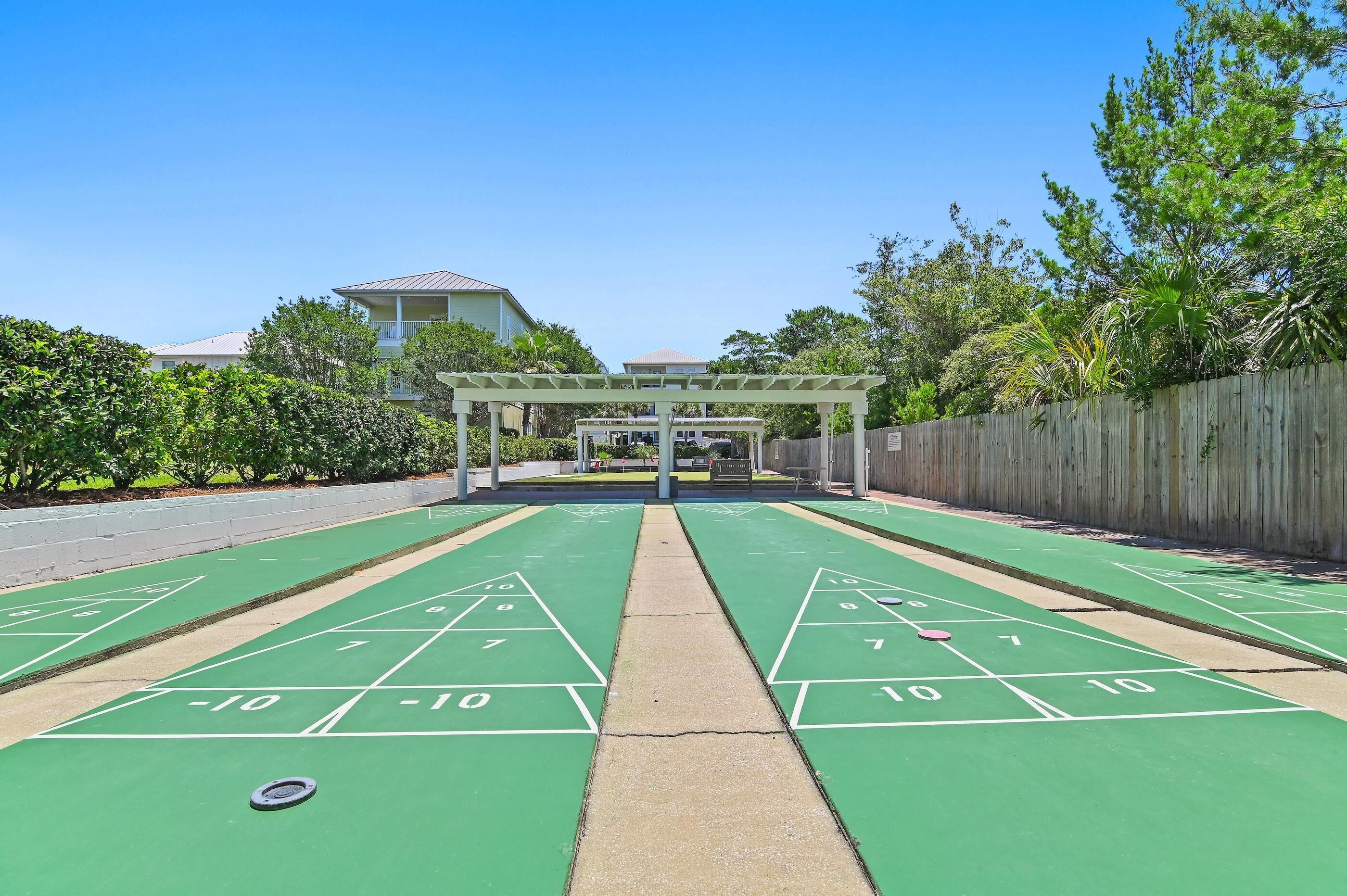 A shuffleboard court with a wooden fence and greenery in the background.