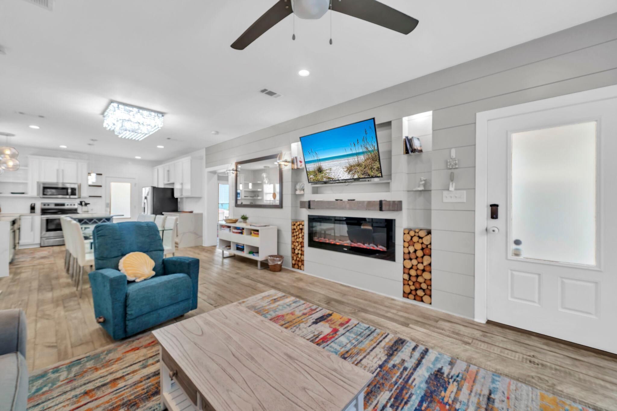 A modern living room with a flat-screen TV, a fireplace, and a dining area with a blue armchair and a wooden coffee table.