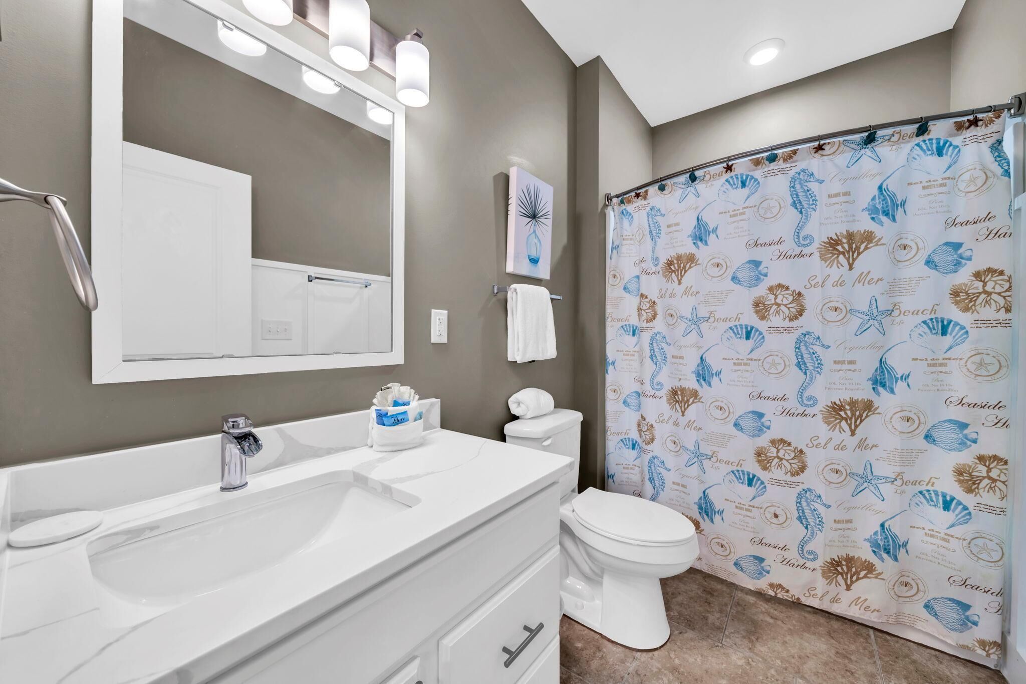 A bathroom with a white vanity, a mirror, a toilet, and a shower curtain with a sea-themed pattern.