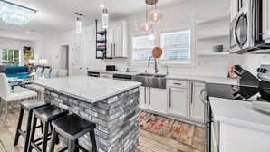 A modern kitchen with a large island, white cabinetry, stainless steel appliances, and pendant lighting. - Kitties Koop (Santa Rosa Beach)
