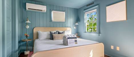 A bedroom with a bed, a ceiling fan, an air conditioning unit, a window with blinds, and a wall-mounted light fixture.