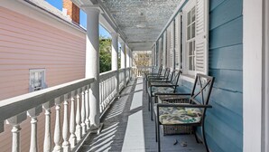 En inglasad veranda med vita räcken och fåtöljer i rotting.