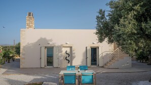 A modern building with a stone chimney, two doors with shutters, and a staircase leading to an upper level.