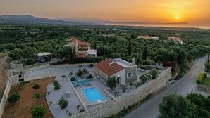 A villa with a swimming pool, surrounded by olive groves and a stone wall.