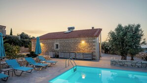 A stone building with a tiled roof, a swimming pool, and blue lounge chairs.