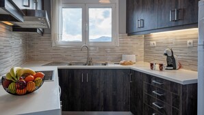 A modern kitchen with dark wood cabinets, a white countertop, a built-in oven, and a window with a view of the mountains. - Aggeliki House Jetted Tub, Vasiliki & Aggeliki (Rethymno)