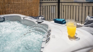 A hot tub with water jets, a glass of orange juice, and a blue towel on a sunlit patio with a bamboo fence and metal railing in the background. - Aggeliki House Jetted Tub, Vasiliki & Aggeliki (Rethymno)
