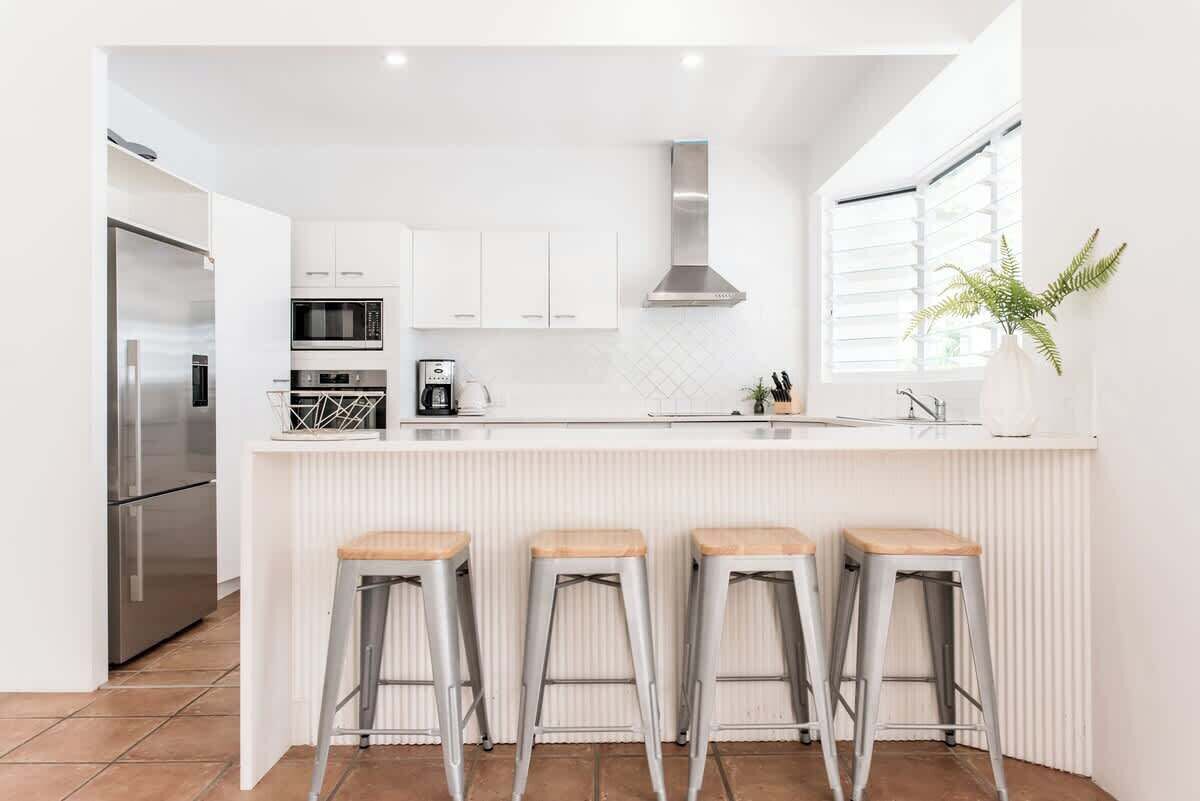A modern kitchen with white cabinetry, a stainless steel refrigerator, a microwave, a coffee maker, and a plant.