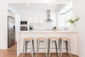 A modern kitchen with white cabinetry, a stainless steel refrigerator, a microwave, a coffee maker, and a plant.
