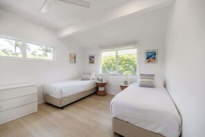 A bedroom with two single beds, a dresser, and a window with blinds.
