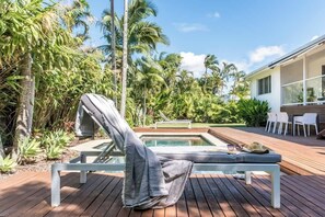 A poolside area with a lounge chair, a small pool, and a deck with chairs and a table. - Pura Vida Noosaville Retreat with Pool (Noosaville)
