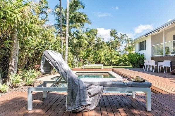 A poolside area with a lounge chair, a small pool, and a deck with chairs and a table.