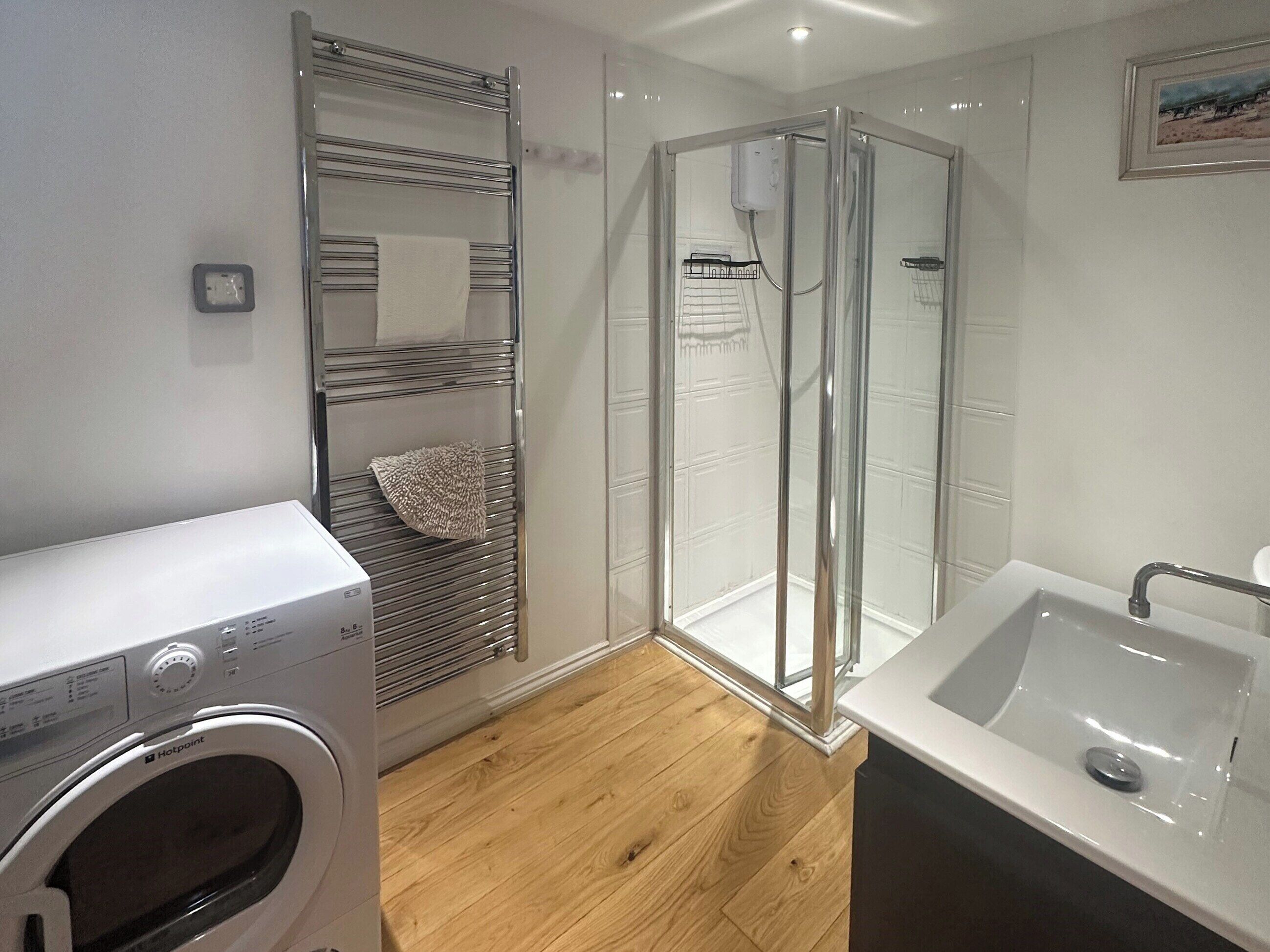 Un baño moderno con ducha de vidrio, lavadora integrada y un espacio separado para el lavamanos.