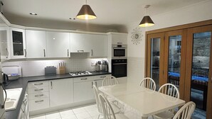 Una cocina moderna con armarios blancos, una estufa a gas y un comedor con mesa y sillas blancas.