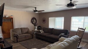 Uma sala de estar com dois sofás, uma mesa de centro, uma televisão e ventiladores de teto.