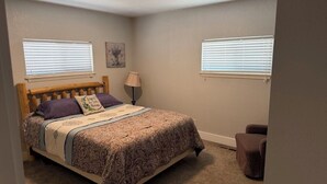 Quarto com cama, duas janelas com persianas, abajur e cadeira.
