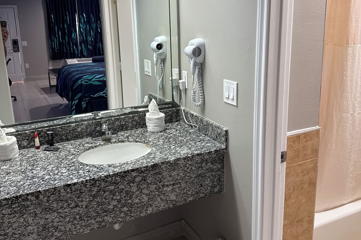 A bathroom with a granite countertop, a sink, two hair dryers mounted on the wall, and a trash can.