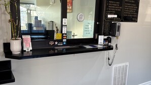 A hotel reception desk with a black counter, a potted plant, and a sign listing room rules. - Scottish inns & suites (Houston)