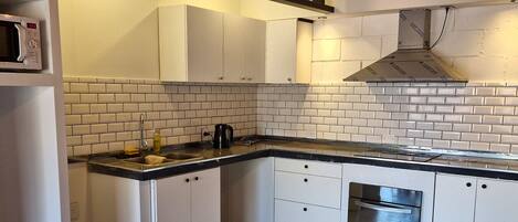 A kitchen with white cabinets, a black countertop, a stainless steel range hood, a microwave, and a refrigerator.