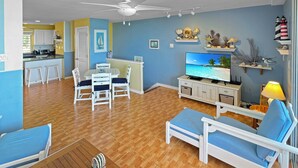 Una sala de estar con televisor, ventilador de techo y comedor con mesa y sillas.