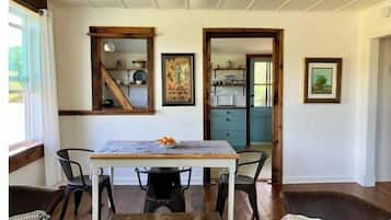 Un coin repas avec une table en bois, quatre chaises et un banc. Deux tableaux encadrés ornent le mur, et une fenêtre est agrémentée de rideaux.