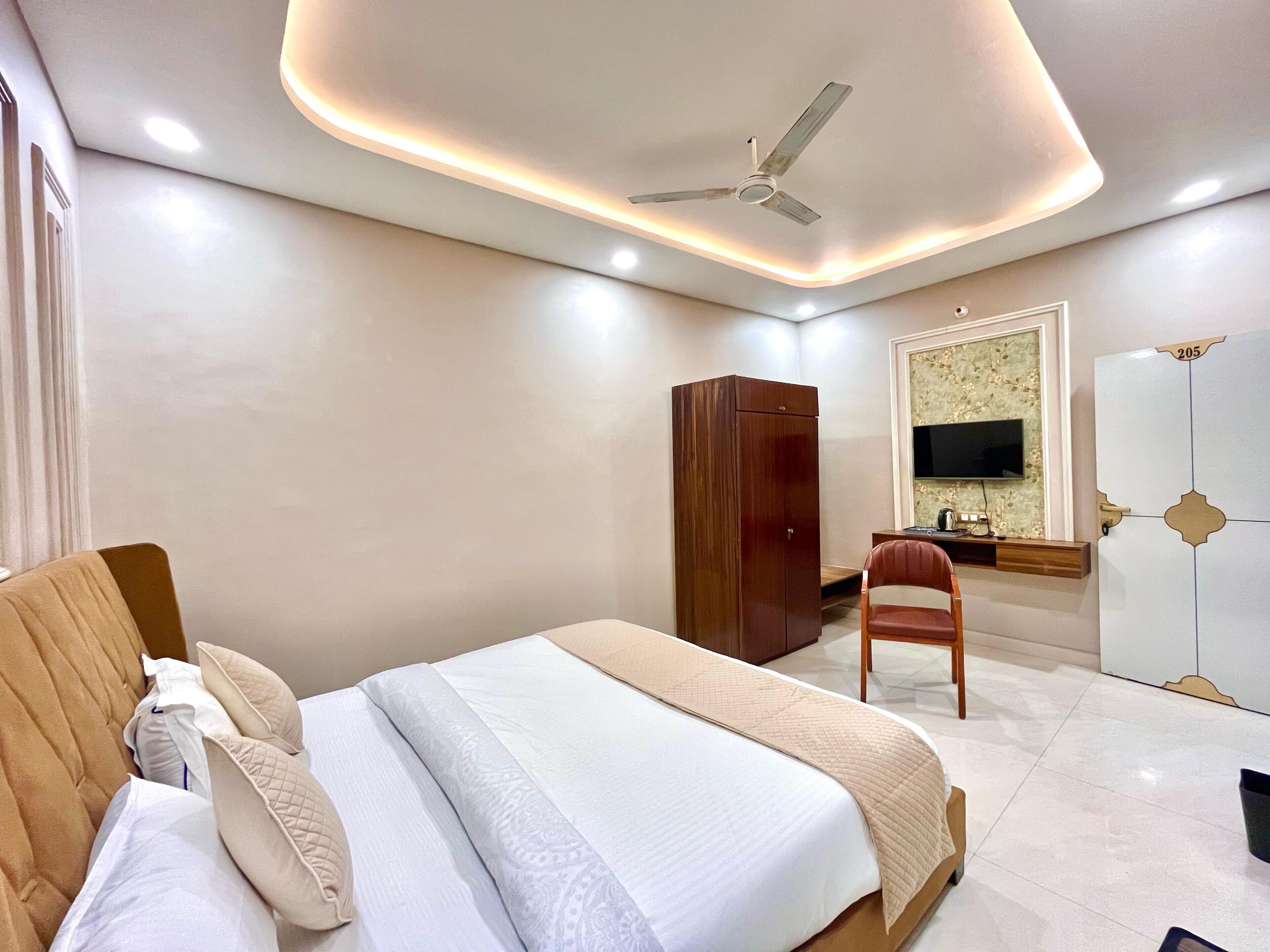 Une chambre d’hôtel comprenant un lit, une armoire, un bureau avec une chaise, une télévision et un ventilateur de plafond.