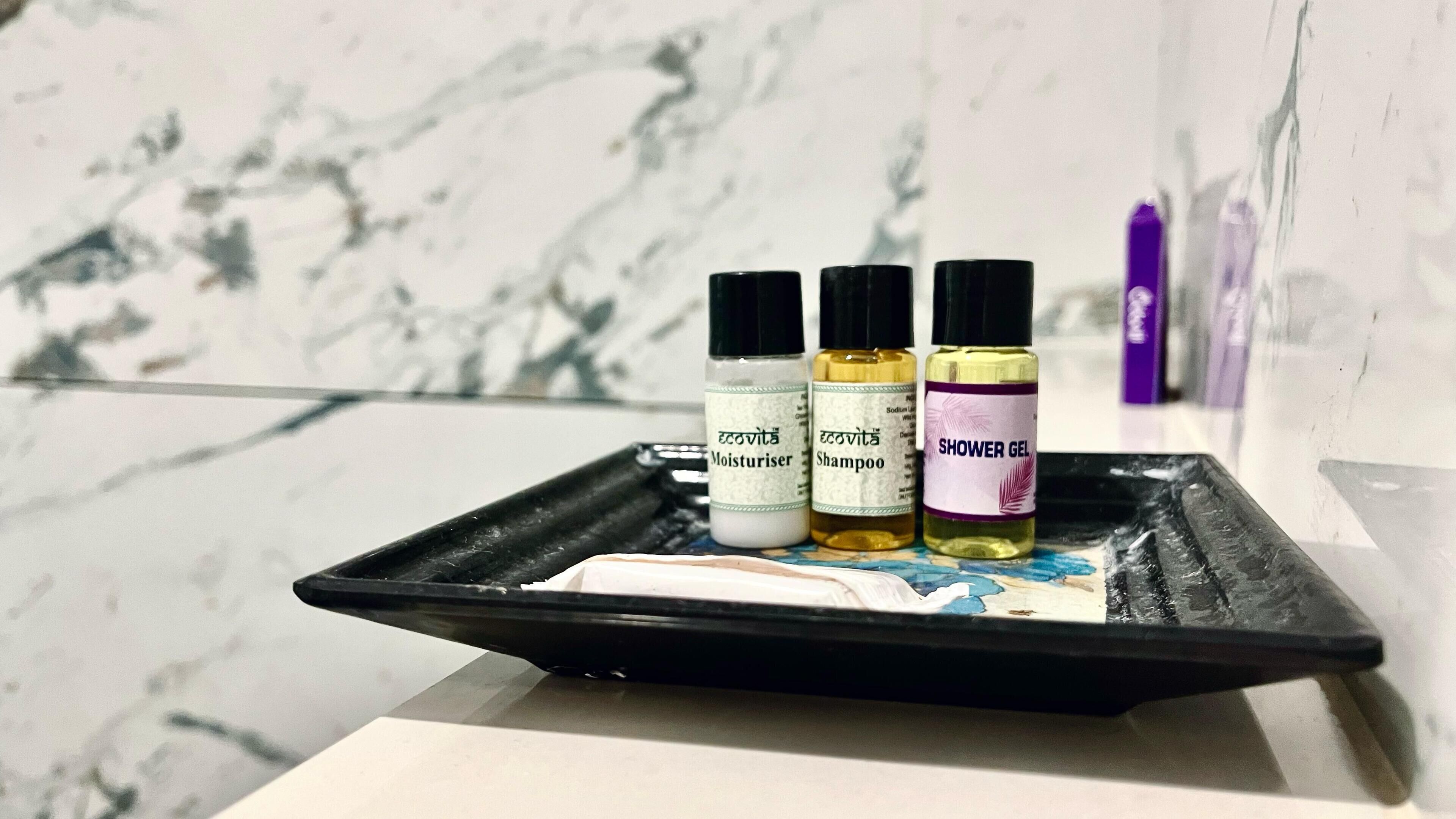 A tray with three bottles of shower gel, a bottle of shampoo, and a bottle of moisturizer on a marble surface.