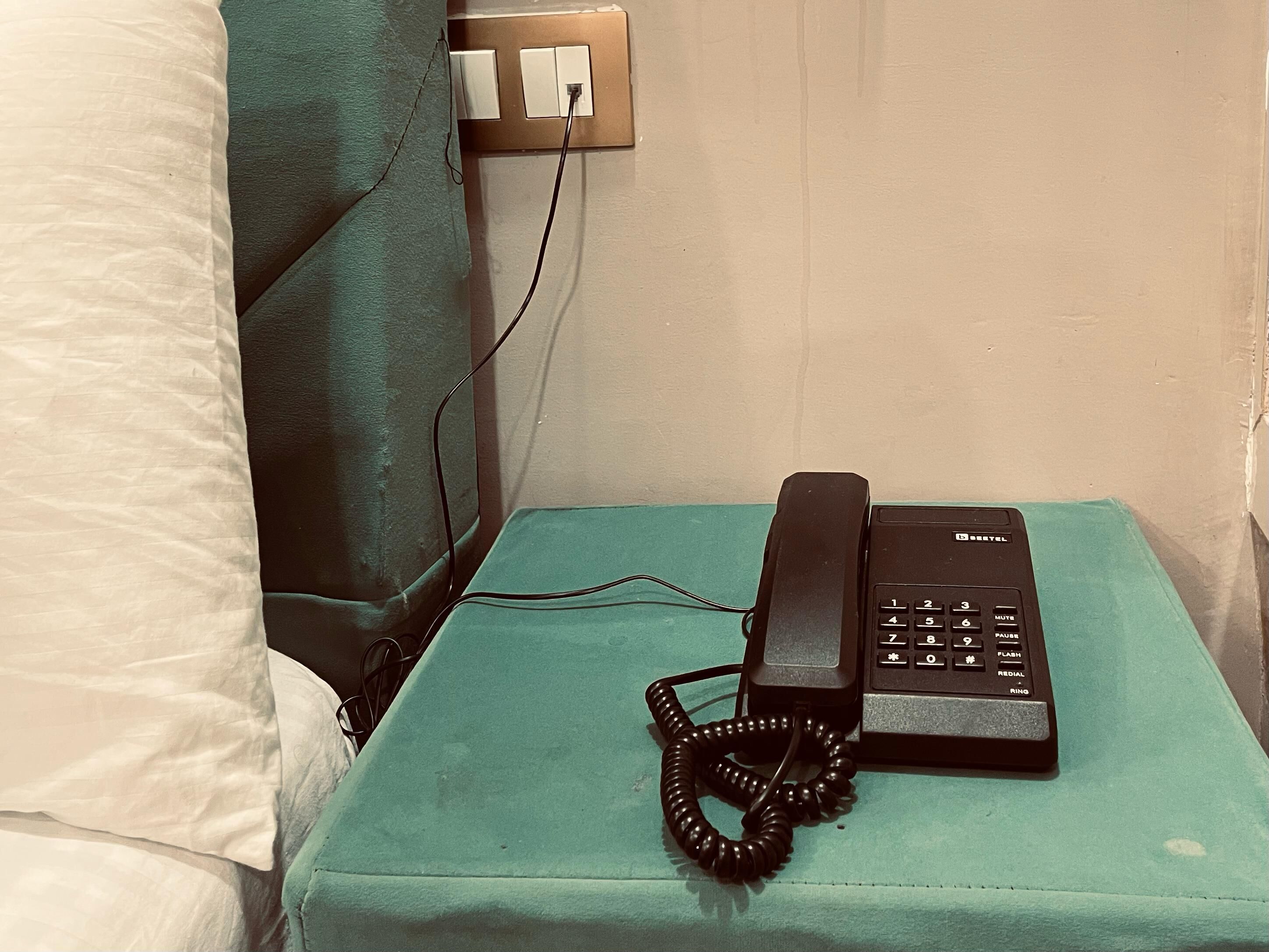 A small bedside table with a black telephone and a coiled cord.