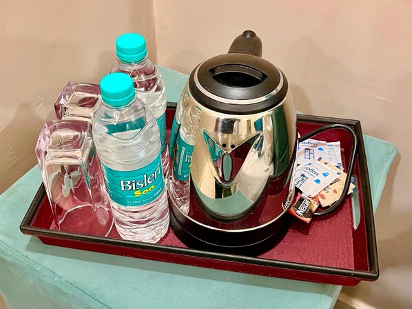 A tray with a water bottle, a glass, a kettle, and some packets. - siyavar palace (Orchha)