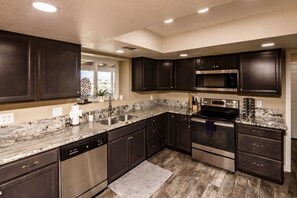 A modern kitchen with dark cabinetry, stainless steel appliances, and a granite countertop.
