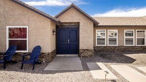 A two-story house with a dark blue front door, a stone foundation, and a gravel driveway. - Havasu Terrace - Pool, Fire Pit, Game Room (Lake Havasu City)