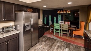 A modern kitchen with dark cabinetry, a stainless steel refrigerator, a built-in oven, and a dining area with a table and chairs. - Havasu Terrace - Pool, Fire Pit, Game Room (Lake Havasu City)