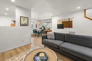 A modern living room with a grey sofa, a dining area, and a kitchen in the background.