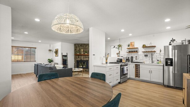 A modern kitchen with white cabinets, a stainless steel refrigerator, and a dining area with a wooden table and chairs. - Lincoln Log Cabin | Renovated | Near Attractions (Big Bear)