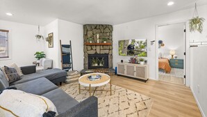 A living room with a stone fireplace, a sofa, a coffee table, and a TV. - Lincoln Log Cabin | Renovated | Near Attractions (Big Bear)