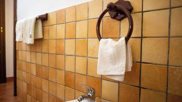 Un baño con pared de azulejos, un lavamanos y dos toalleros con toallas blancas.