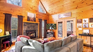 A cozy cabin interior with a fireplace, wooden walls, a sofa, and a dining area.