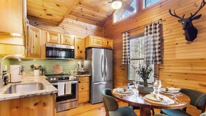 A wooden cabin interior with a kitchen, dining area, and a mounted deer head.