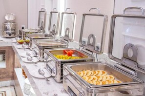 Monipuolinen buffetpöytä, jossa on useita ruokatarjoilupisteitä sekä laaja valikoima erilaisia ruokia ja ruokailuvälineitä.