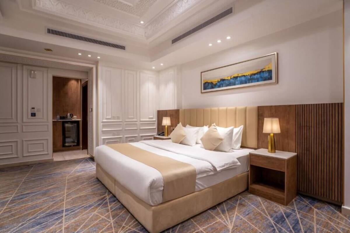 Ein Hotelzimmer mit einem großen Bett, zwei Nachttischen mit Lampen, einem Bild an der Wand und einem gemusterten Teppich.