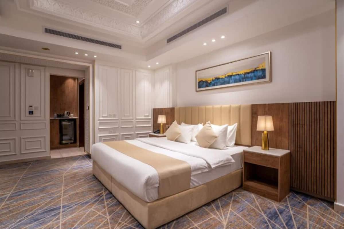 A hotel room with a large bed, two bedside tables with lamps, a painting on the wall, and a patterned carpet.