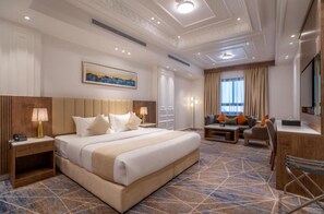 A hotel room with a large bed, a desk, a chair, a TV, and a painting on the wall. - Nars Plus Al Naeem Hotel (Jeddah)